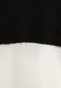 Fekete bordázott kötött anyag, ami sima fehér anyagra vált. A felső rész texturált, míg az alsó sima, enyhe fényével.