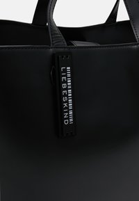 Czarna torba na ramię wykonana z gładkiego materiału, posiadająca podwójne uchwyty oraz prostokątną metkę z napisem "LIEBESKIND" w białym kolorze.