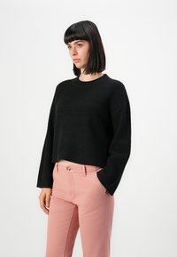Svart kortstickad tröja med en texturerad, våfflad stickning, i kombination med ljusrosa raka byxor med framficka.