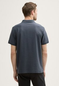 Ciemnoszara koszulka polo z krótkim rękawem, wykonana z teksturowanej tkaniny, z klasycznym kołnierzykiem i prostym wykończeniem. Brak widocznych logo lub wzorów.