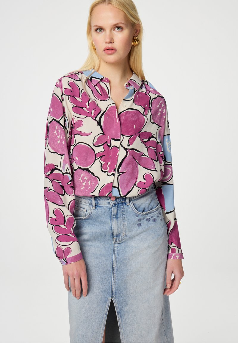Multikleurige blouse met een roze bloemenpatroon, knoopsluiting aan de voorkant en een lichtblauwe kraag; gecombineerd met een spijkerrok tot de knie met een split aan de voorkant.