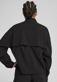 Sort jakke med en løs pasform, featuring et lagdelt bagdesign, elastiske manchetter og en glat, let stofstruktur.