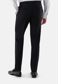 Schwarze Hose mit maßgeschneidertem Schnitt, ausgestattet mit zwei Rückentaschen mit Knöpfen, einer glatten Textur und geradem Bein. Abgebildet mit schwarzen Schuhen.