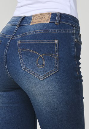 Donkerblauwe jeans met een lichte vervaging, voorzien van een tanleren label, gouden stiksels op de zakken en een uniek stikselschema.