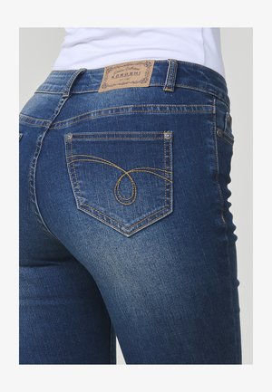 Tumed sinised teksad, millel on kerge kulumine, pruun nahktembeldus, kuldsed õmblused taskutel ja ainulaadne õmblusmuster.