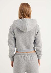 Felpa corta in tessuto felpato grigio chiaro con cappuccio regolabile e polsini a coste; abbinata a pantaloni della tuta grigi con vita elastica.
