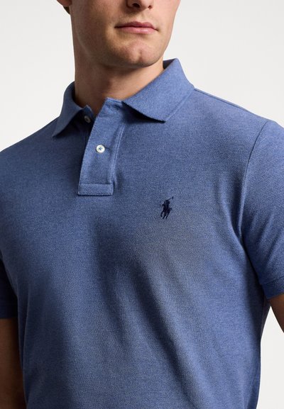 Polo krekls tumši zilā kokvilnas maisījumā ar teksturētu virsmu. Iekļauj apkakli, divu pogu slēgšanu un mazu izšūtu logotipu uz krūšu.