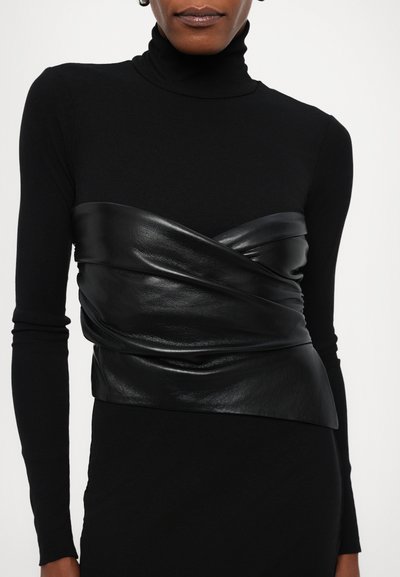 Haut à col roulé noir à manches longues superposé avec un wrap en cuir noir brillant accentuant la taille, présentant une texture lisse et un design ajusté.