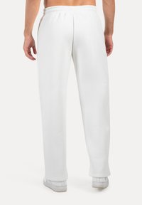 Weiße Jogginghosen aus weichem Stoff, mit geradem Schnitt, elastischem Taillenbund und ohne sichtbare Taschen, kombiniert mit weißen Turnschuhen.