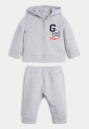 Hellgrauer Kapuzenpullover für Kleinkinder mit Reißverschluss und passender Hose mit elastischem Bund, der Kapuzenpullover ist mit baseballbezogenen "G Guess"-Patches auf der Brust versehen.
