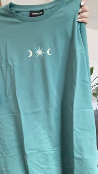 Camiseta de algodón azul turquesa de manga corta, que presenta un gráfico central de un sol y lunas crecientes en blanco y amarillo.