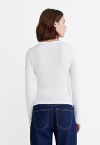 Valkoinen pitkähihainen slim fit -paita, jossa on ribbikuvio. Paidassa on pyöreä pääntie. Yhdistetty tummansiniset korkeavyötäröiset farkut, joissa on takataskut.