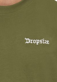 Oliven grønn t-skjorte i bomull, med rund hals og hvit brodert tekst "Dropsize" på venstre brystområde.