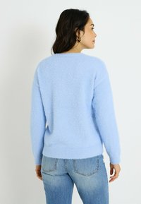 Suéter azul claro, esponjoso, con un ajuste relajado, dobladillo y puños acanalados. Combina con vaqueros de lavado medio, mostrado desde atrás.