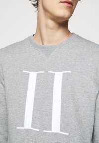 Szara bluza z bawełny, z dużym białym nadrukiem "II" na przodzie. Dekolt typu crew z prążkowanym wykończeniem.