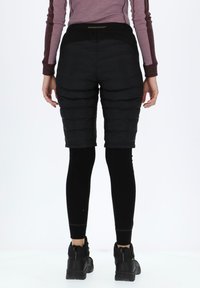 Zwarte geïsoleerde shorts met een gequiltde structuur, gedragen over zwarte leggings. De taille is voorzien van een merkembleem elastische band.