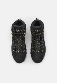 Un par de botas de senderismo negras con cordones acentuados en amarillo, cuellos acolchados y suelas resistentes, fotografiadas desde arriba sobre un fondo blanco.