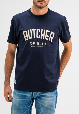 Navyblauwe katoenen t-shirt met korte mouwen, voorzien van een crème kleurige afbeelding met de tekst "BUTCHER OF BLUE" en een klein merklogo aan de zoom.