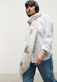 Hele sinine lillemustriga sall, millel on roosad ja rohelised mustrid, valmistatud pehmest ja kergest kangast, mis on vabal moel mudeli kaela ümber laotud.