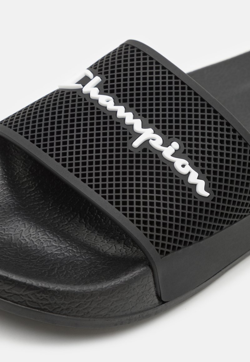 Schwarze Flip-Flop-Sandale mit einer strukturierten Gummisohle, die ein perforiertes Oberband und ein weißes "Champion"-Logo zur Markenkennzeichnung aufweist.