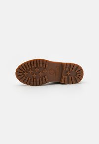 Sola de bota de borracha castanha com profundos sulcos e um logotipo. Apresenta padrões horizontais e verticais para tração e aderência.
