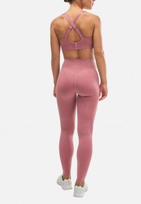 Sujetador deportivo rosa con tirantes en forma de cruz en la espalda, combinado con leggings rosas de cintura alta. Ambos elaborados con un tejido suave y elástico. Zapatillas blancas.