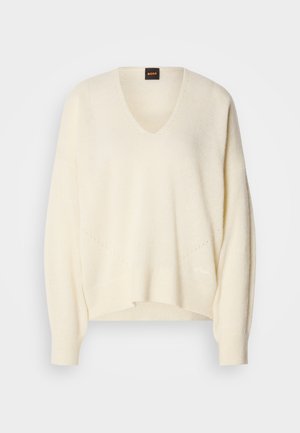 Grietos V formos megztinis, pagamintas iš minkštos medžiagos, su plačiomis rankovėmis, laisvu siluetu ir subtiliais megztiniais akcentais apykaklėje ir petyse.