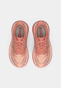 Hoka One One löparskor i korallrosa med en texturerad meshuverdel, framträdande snörningssystem och vadderad sula för ökad komfort.