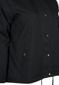 Veste noire avec fermeture à boutons-pression, poches latérales à boutons-pression, poignets élastiqués, et cordons de serrage à la capuche et à l'ourlet.