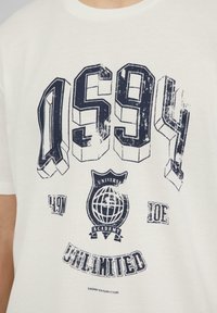Witte katoenen T-shirt met gedurfde marineblauwe grafische tekst "OS94," een wereldbol-embleem en de woorden "UNIVERSITY ACADEMY" en "UNLIMITED."