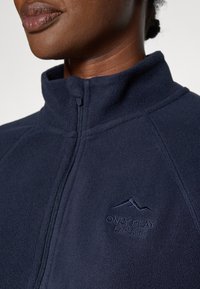 Mornarska flis jakna na zip s visokim ovratnikom, izvezenim logotipom planine i šavnim detaljima na ramenima. Mekana tekstura.