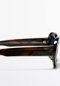 Occhiali da sole a forma di tartaruga marrone con una montatura ampia, lenti scure, forma elegante e dettagli incisi sulla tempia, etichettati con protezione UV.
