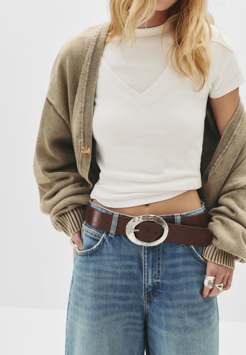 Svetlohnedý kardigán cez biely top s krátkym rukávom, kombinovaný so svetlomodrými džínami. Tmavohnedý opasok so striebornou oválnou sponou a prsteňmi.