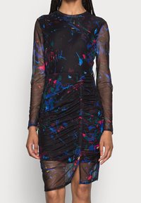 Zwarte jurk met lange doorschijnende mouwen, voorzien van kleurrijke spetterpatronen, geplooide textuur en een hoge split tot boven de dij. Zachte stofafwerking.