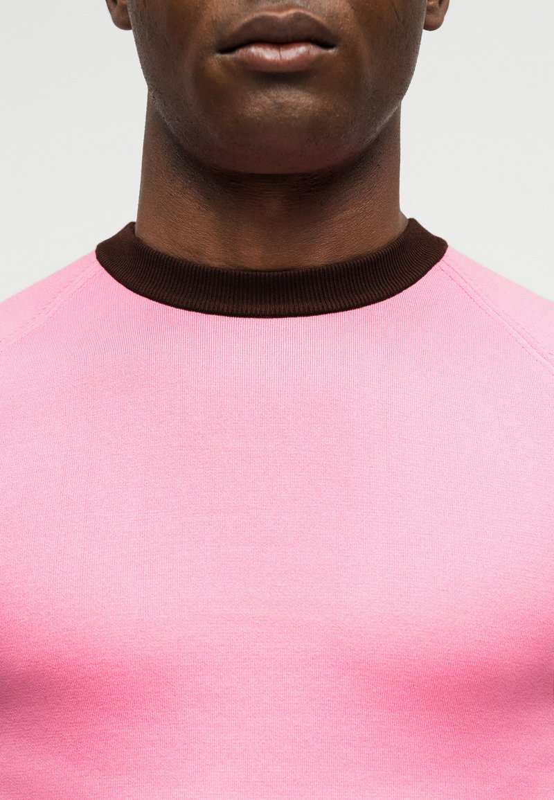 Close-up of a person wearing a pink crew neck shirt with a dark brown collar, showing the lower face and neck area.
