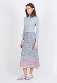 Kvinde iført en lys blå ribbet turtleneck, mønstret midi-nederdel med blå og pink designs, og lysegrå sneakers med hvide accenter.