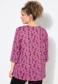 Top rosso e blu con motivo, dalla vestibilità morbida, maniche 3/4 e scollatura rotonda, realizzato in tessuto leggero. Pantaloni neri indossati sotto.