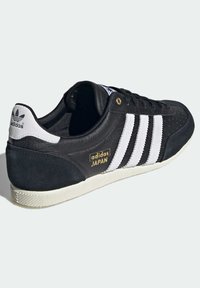 Black leather and suede sneaker with white stripes, gold "adidas JAPAN" logo, textured side, tonal laces, and rubber sole.