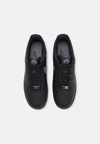 Czarne sneakersy Nike Air Force 1 z gładką skórzaną cholewką, okrągłym noskiem, perforacjami, sznurowanym zapięciem oraz srebrnymi akcentami na języku.