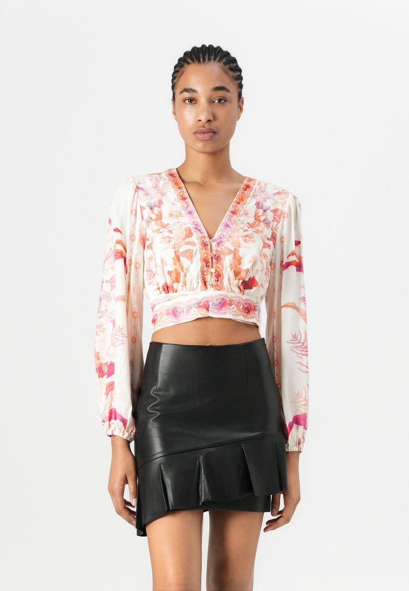 Blumenmuster-Crop-Top aus leichtem Stoff mit langen PuffÄrmeln und V-Ausschnitt, kombiniert mit einem figurbetonten schwarzen Miniskirt aus Leder mit Rüschen.