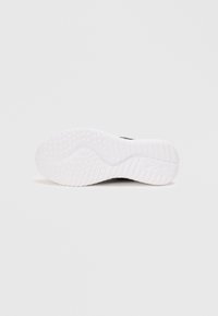Svart sneaker med en teksturert hvit gummisåle, som har et bølgete mønster og gripe detaljer for godt feste. Overdelen er slank og glatt.