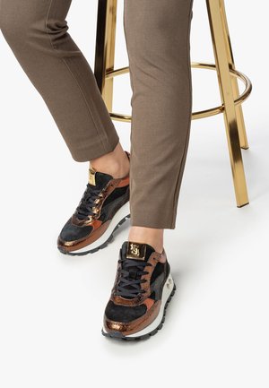 Sneaker multicolore con una combinazione di camoscio nero, accenti metallici bronzo e una suola bianca con battistrada a motivo. Dettaglio del logo dorato sulla linguetta.