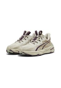 Zapatillas deportivas beige con un upper texturizado, acentos morados y una suela media voluminosa. Presentan un sistema de cordones reforzado y un diseño con patrón.