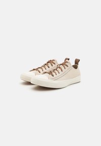 Beige vászon sneaker barna fűzőkkel és szövet fogantyúval. Lekerekített orr, texturált fehér gumitalppal, finom varrás részletekkel.