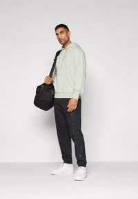 Light green hoodie with a front pocket, paired with black tapered pants featuring zipper accents. White sneakers and a black slouchy bag.