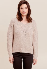 Helles beiges Strickoberteil mit V-Ausschnitt, weit geschnittenen Ärmeln und dekorativen Mustern. Weiche Textur mit gerippten Bündchen und Saum.