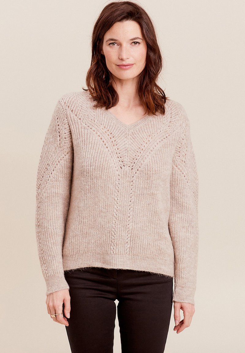 Helles beiges Strickoberteil mit V-Ausschnitt, weit geschnittenen Ärmeln und dekorativen Mustern. Weiche Textur mit gerippten Bündchen und Saum.