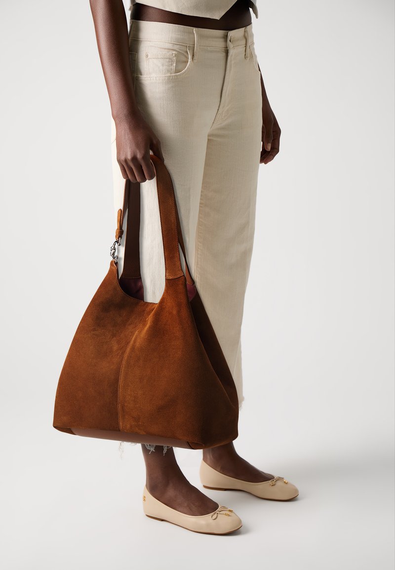 Sac hobo en suède marron avec une large ouverture et une courte poignée, présentant une texture lisse et une doublure contrastante visible à l'ouverture.