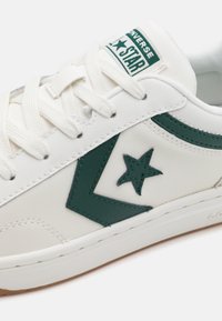 Biele kožené tenisky s zelenou hviezdou ako akcentom a zodpovedajúcim bočným pruhom. Zaoblená špička a textúrovaná gumová podrážka pre lepšiu priľnavosť.