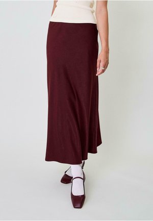 Fustă lungă, fluidă, de culoare bordeaux, fabricată dintr-un material moale. Prezintă o textură fină, un strălucire subtilă și un talie medie. Asortată cu pantofi maroni.